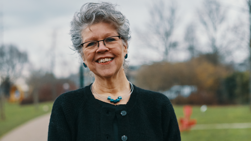 Foto van Statenlid Ariette Kasbergen, ze draagt een zwart vest en heeft kort grijs haar en lacht in de camera. Op de achtergrond een stadspark in Leiden